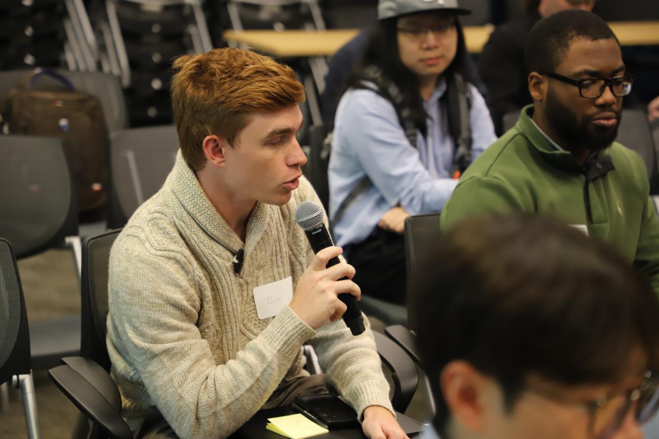 A male student attendee holding a microphone asks a question during one of the symposium's panel discussions.