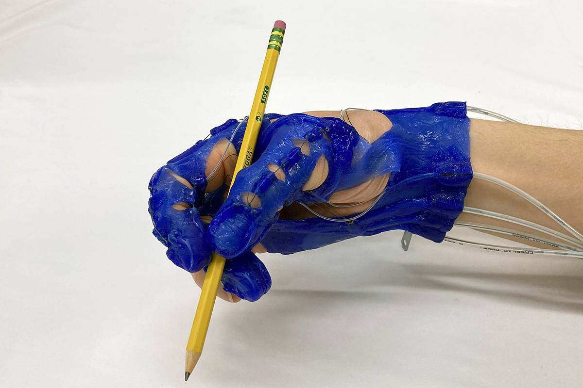 Blue hand exoskeleton glove gripping a pencil