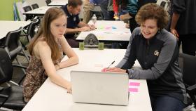 Cristi Bell-Huff, right, and a student look at a laptop on a table in the midst of a class session. 