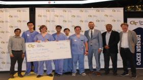Photo of five male students from Capstone team One-Hand Wonder along with their sponsor on the right, undergraduate chair Jaydev Desai on the far right, and another guest on the far left. The students are standing together with a large check their hand for $3,000.