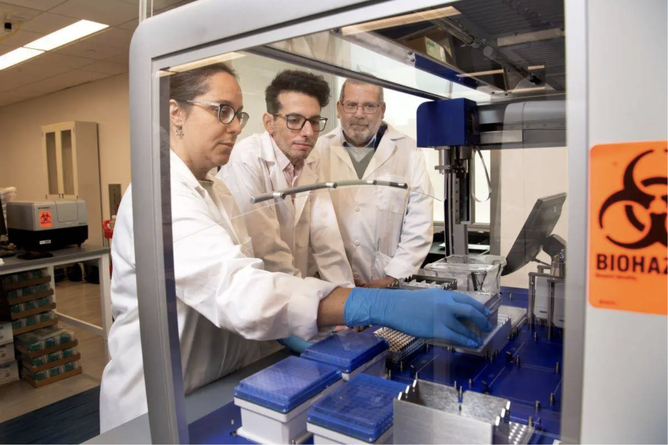 From left, Lorena Chaves, Jose Assumpcao, and Philip Santangelo are standing in a lab examining mRNA samples.