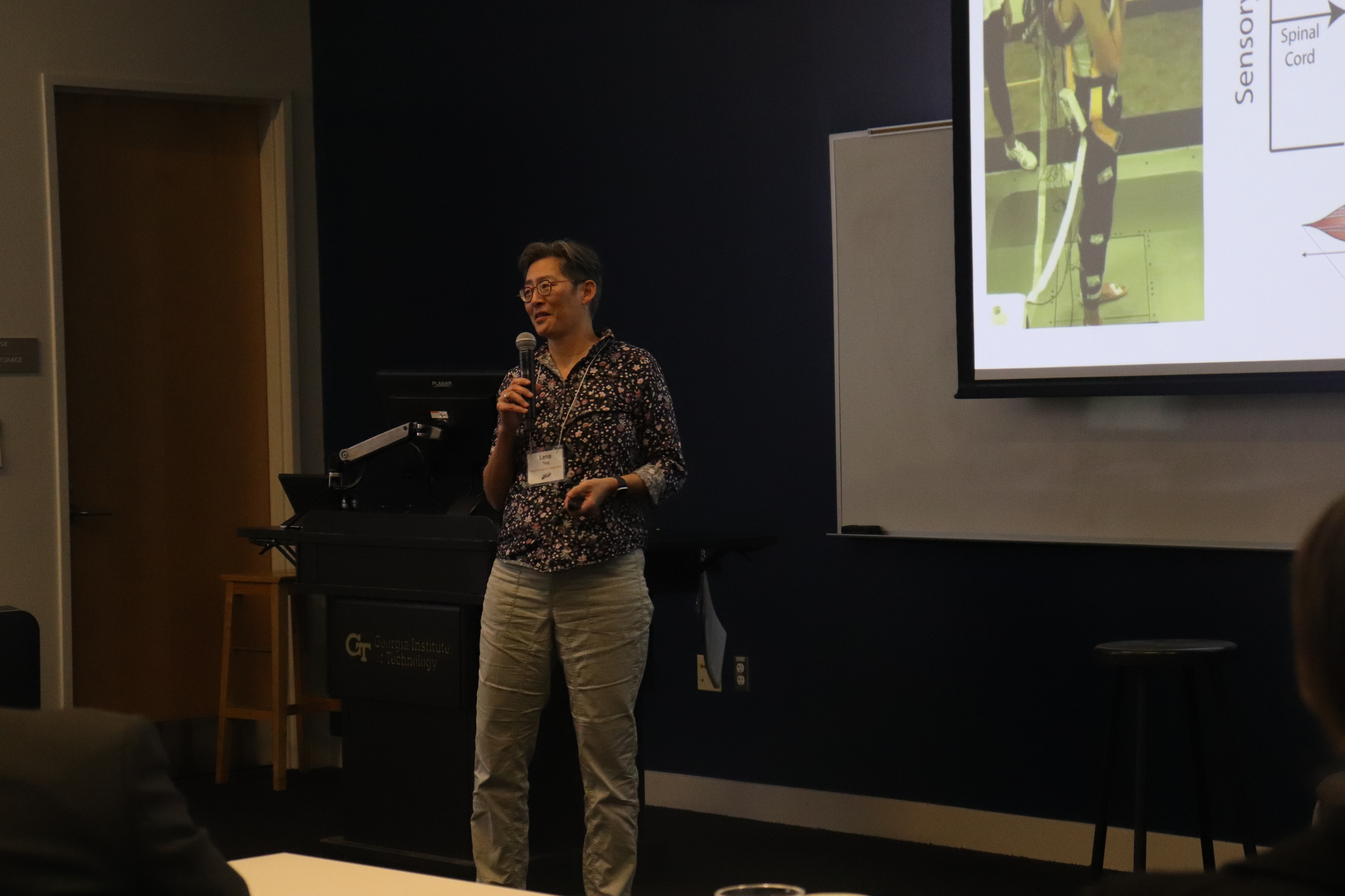 Prof. Lena Ting standing in front of a projection screen speaking