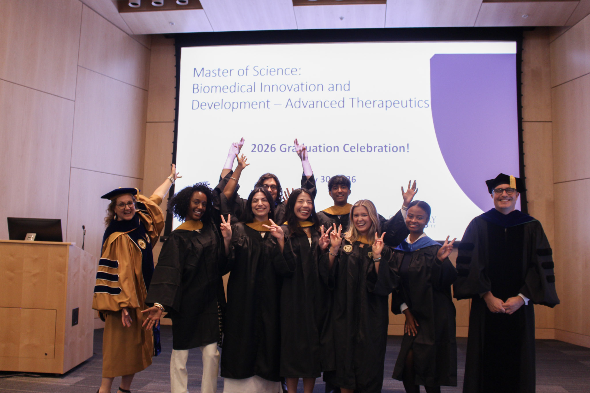 Graduates of the MBID-AT program inside of the auditorium at Emory University posing in their caps and gowns with their program director.