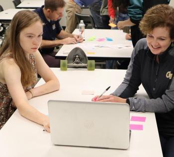 Cristi Bell-Huff, right, and a student look at a laptop on a table in the midst of a class session. 