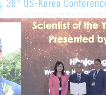 Photo of Prof. Hanjoon Jo in the center holding his Scientist of the Year award flanked by a man and woman, organizers of the ceremony