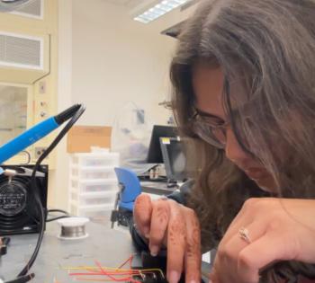 Photo of BME student Bobby Patel wiring a device in a lab. She is working on the device on a lab table.