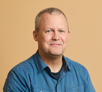 A portrait of a man wearing a blue collared shirt against a gold background