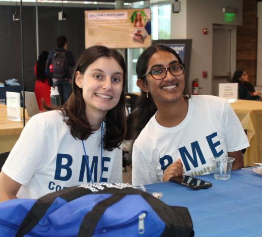 Photo of two female BME students who are volunteers for BME Community Day in 2023 sitting at a table looking directly at the camera for a photo