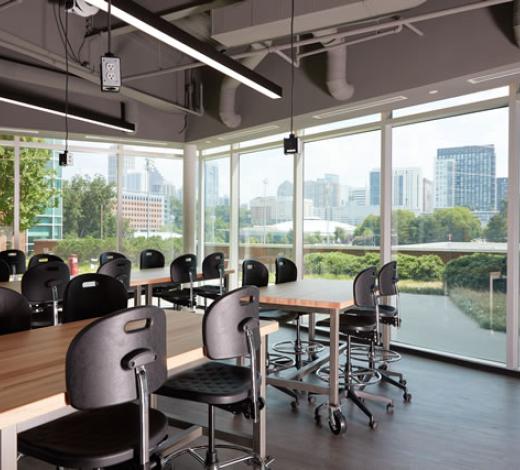 Photo of a group of long tables with chairs facing toward floor length windows of the BME Design Garden
