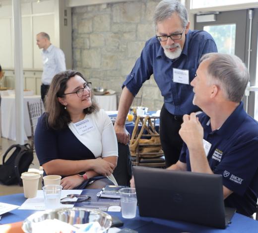 Photo of a group of faculty and staff (one man standing and one woman and one man sitting) talking during the 2024 BME retreat
