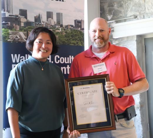 Photo of Emory Dept. Administrator Maita Diaz (left) standing with Lead Developer Steven Marzec who is holding a staff recognition certificate 