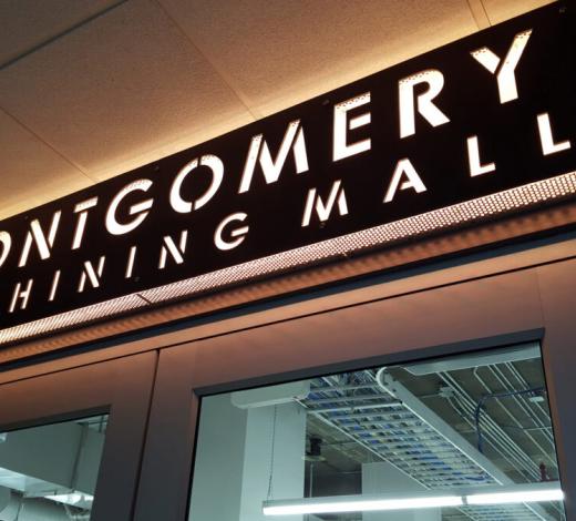 Photo of a glowing sign that says "Montgomery Machining Hall" that sits above the opening door to the space