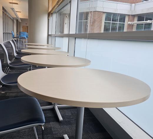 Photo of a group of round tables and chairs in the foreground leading down a glass enclosed walkway of the U.A. Whitaker Building at Georgia Tech.