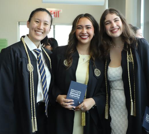 Photo of three students in their graduation regalia posing and smiling for a group photo.
