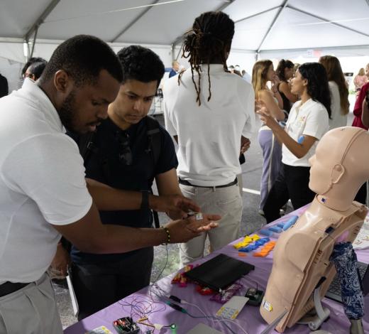 Photo of a Capstone student in a tent area explaining his team's device to an onlooker at GT Capstone Expo.