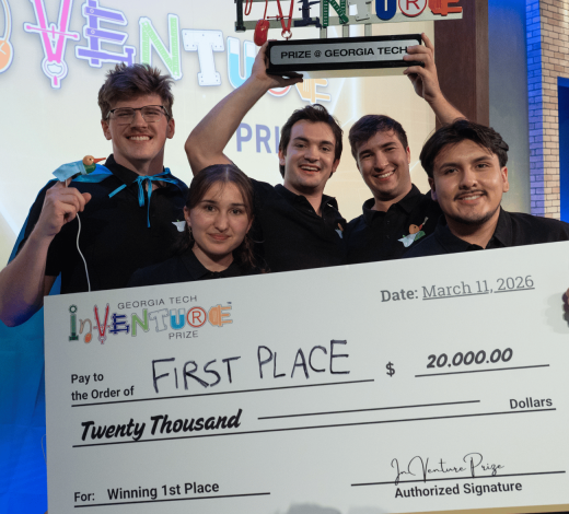 Five members of the winning Georgia Tech InVenture Prize team pose onstage holding a large ceremonial check for $20,000 and a trophy labeled “Prize @ Georgia Tech.” The oversized check reads “First Place” and “Winning 1st Place,” with the Georgia Tech InVenture Prize logo displayed prominently in the foreground. Colorful InVenture Prize signage appears in the background.