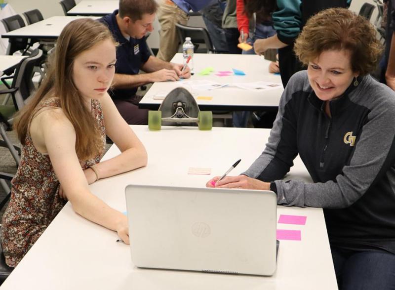 Cristi Bell-Huff, right, and a student look at a laptop on a table in the midst of a class session. 
