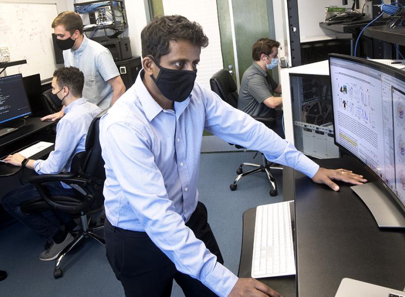 Chethan Pandarinath works at a computer in his lab with students and other researchers working in the background. (Photo: Jack Kearse)