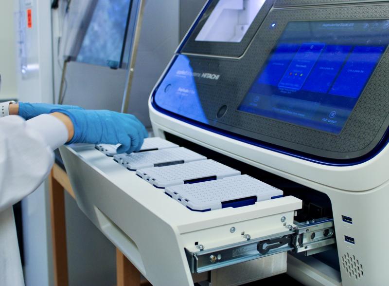 A hand with a blue glove placing a pipette tip tray into the Sanger Sequencing Machine