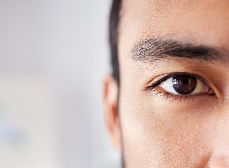 close up of man's brown eye. His dark eyebrows, dark hair, and ear are visible