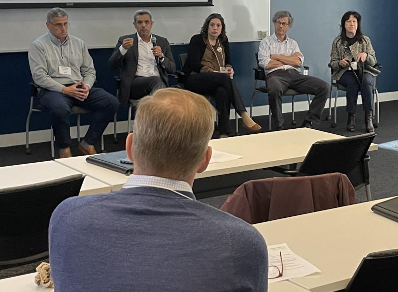 Photo of five McCamish conference panelists. Four panelists (one man and three women) listen to the fourth participant, a male, speaking.