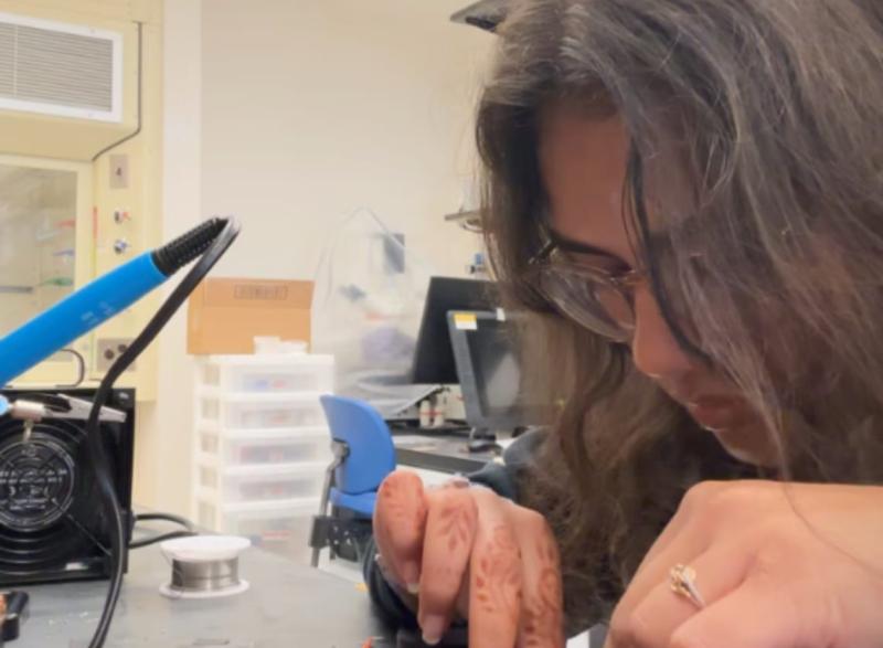 Photo of BME student Bobby Patel wiring a device in a lab. She is working on the device on a lab table.