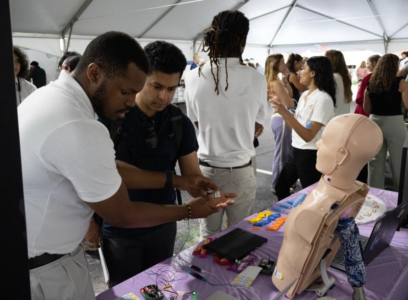Photo of a Capstone student in a tent area explaining his team's device to an onlooker at GT Capstone Expo.