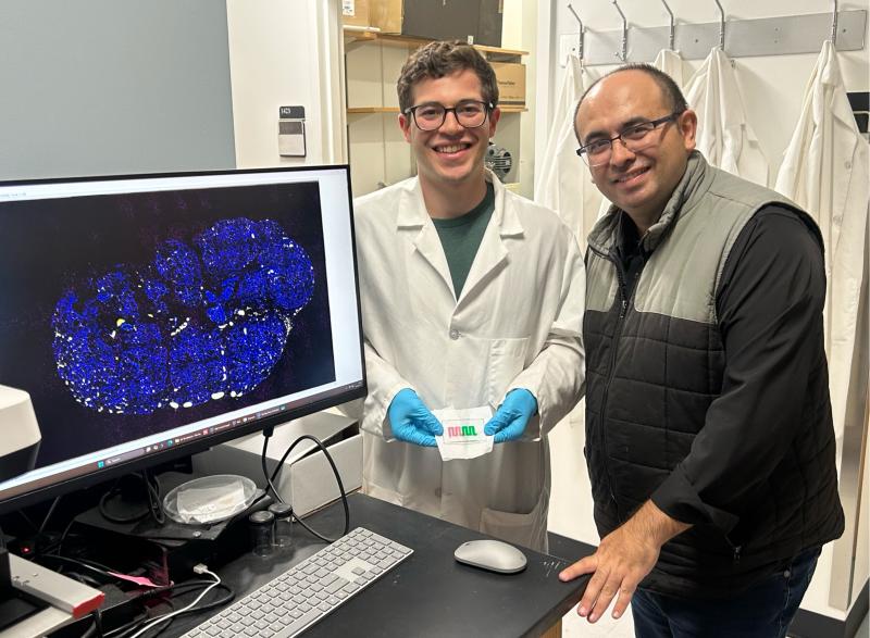 Photo of Dr. Ahmet Coskun and his lab research student hold the "diet-on-a-chip" device.