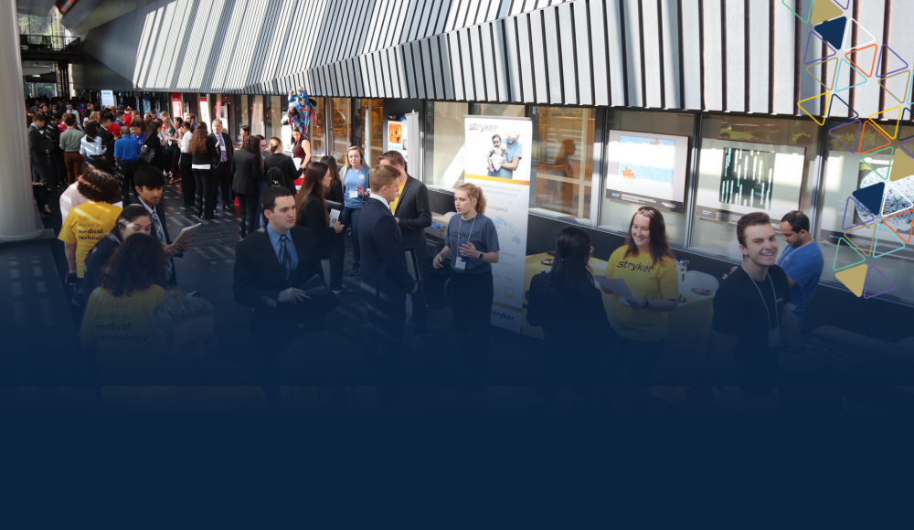 Graphic featuring a photo of an overhead shot looking down on BME students talking to employers. 