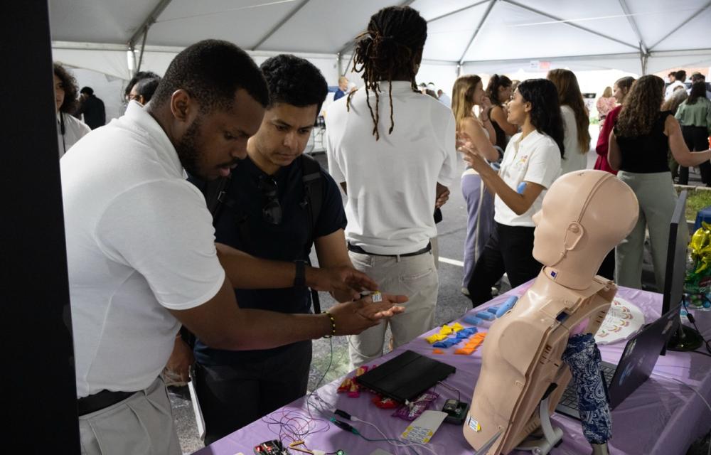 Photo of a Capstone student in a tent area explaining his team's device to an onlooker at GT Capstone Expo.